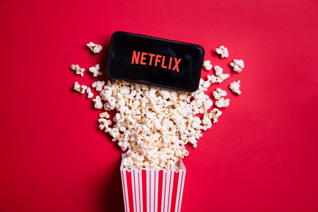 Logo do netflix no celular com um balde de pipoca derramado em um fundo vermelho