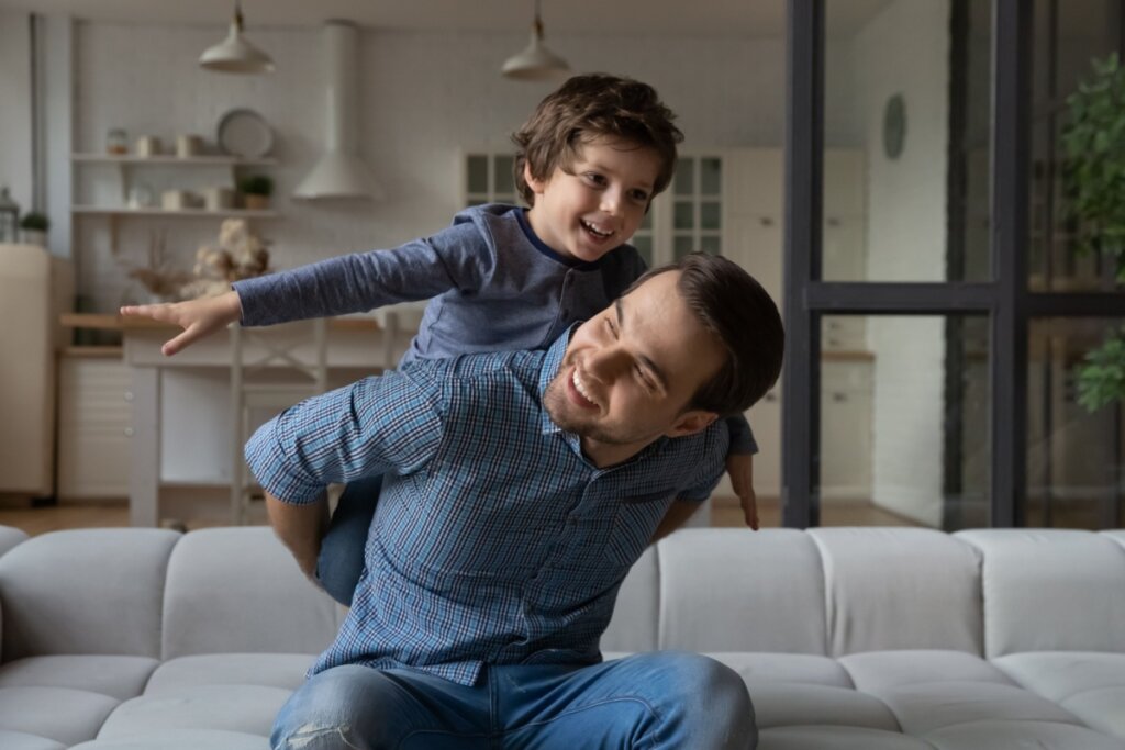 Pai brincando com filho nas costas em uma sala