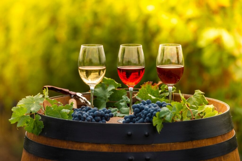 3 taças de vinho em cima de um barril com uvas 