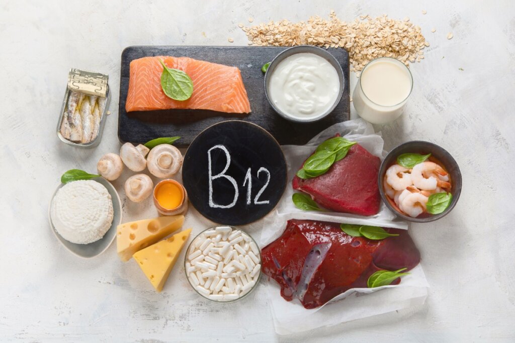 Variedade de alimentos ricos em vitamina B12, incluindo salmão, sardinhas, fígado, camarão, queijos, iogurte, ovos, cogumelos e leite, disposta em uma superfície