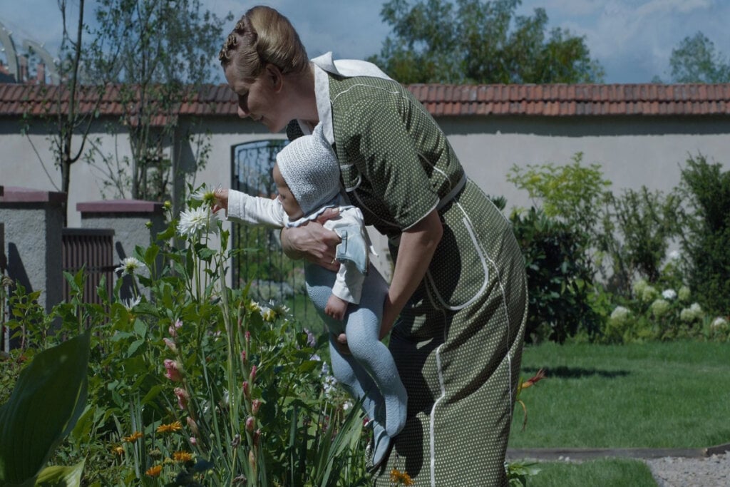 Cena do filme "Zona de Interesse"; mulher e bebê em jardim