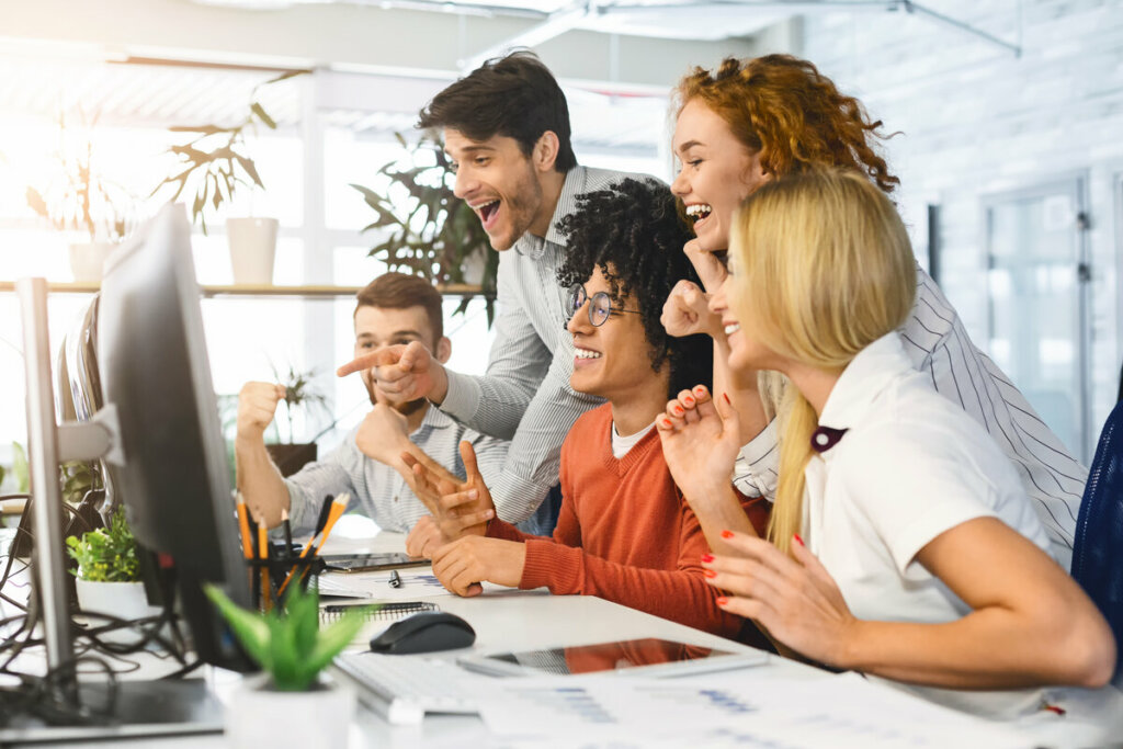 Pessoas em frente a um computador em um escritório sorrindo felizes