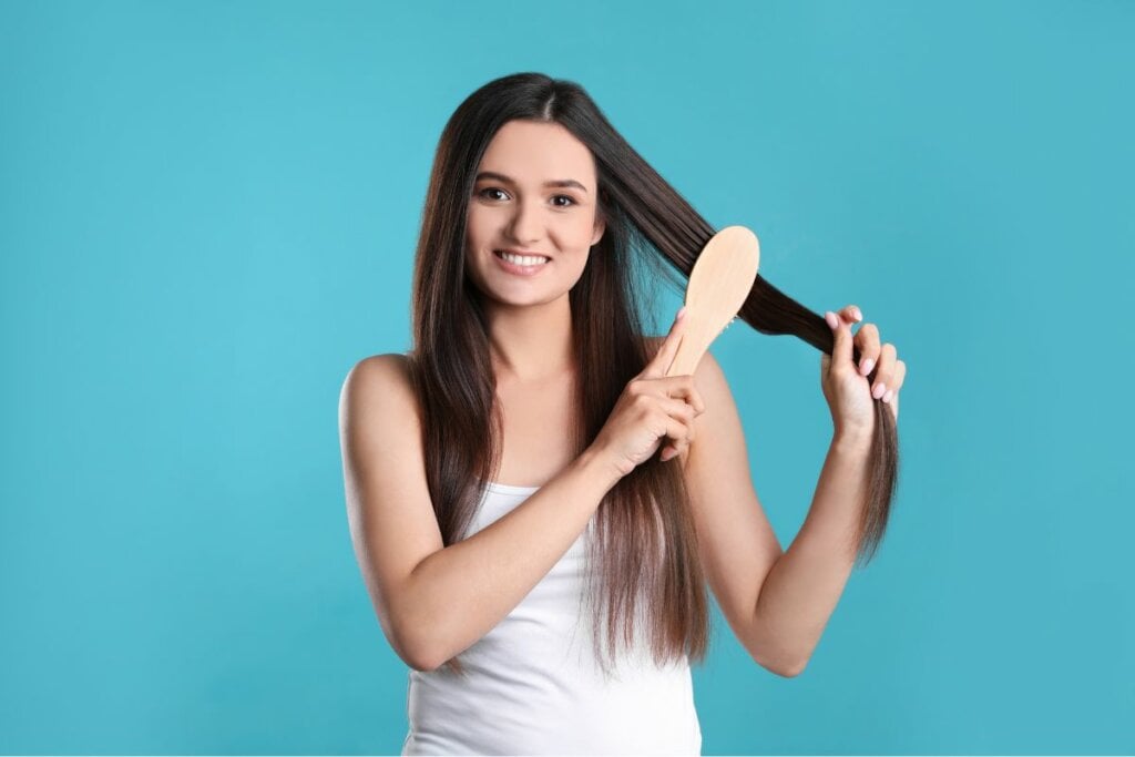 Mulher sorrindo e passando uma escova no cabelo