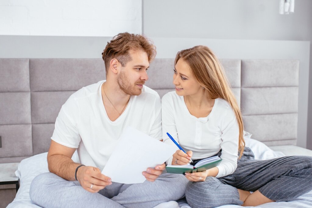 Casal sentado em uma cama e escrevendo em um caderno