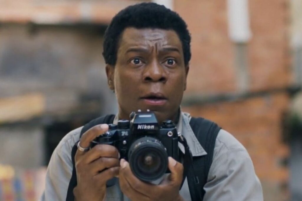 Alexandre Rodrigues como "Buscapé" em "Cidade de Deus: A Luta Não Para" segurando uma câmera fotográfica 