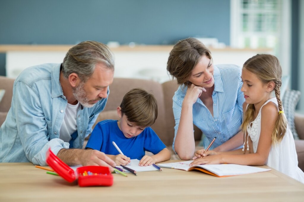 Um homem e uma mulher ao lado de um menino e uma menina sentados desenhando em uma cozinha