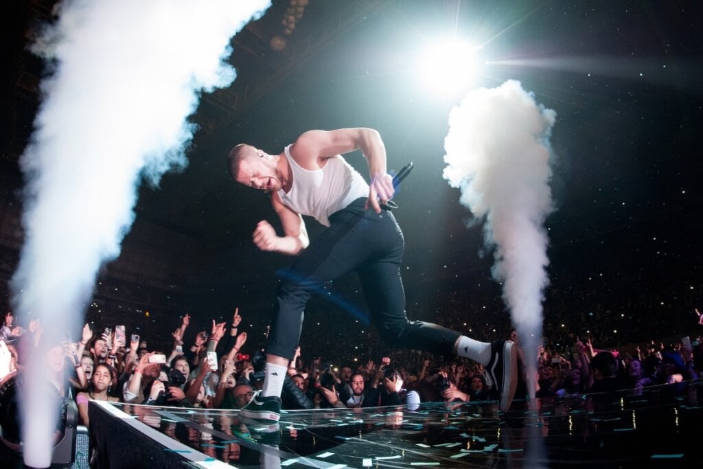 O cantor Dan Reynolds cantando em um palco com fumaça branca 