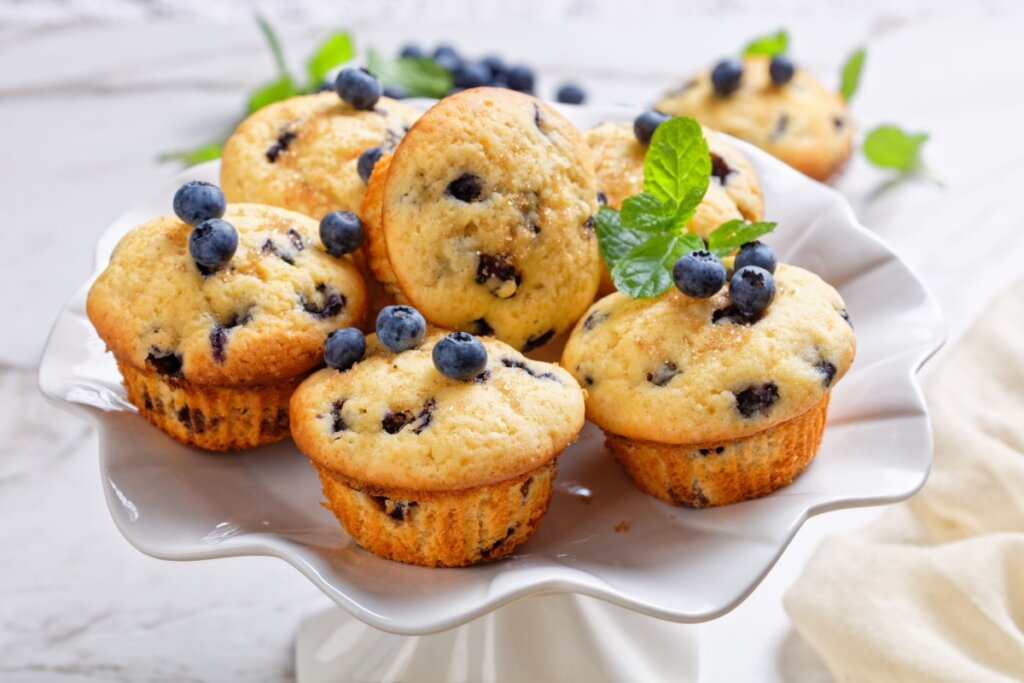 Seis muffins de mirtilos empilhados em prato branco e com folhas de hortelã