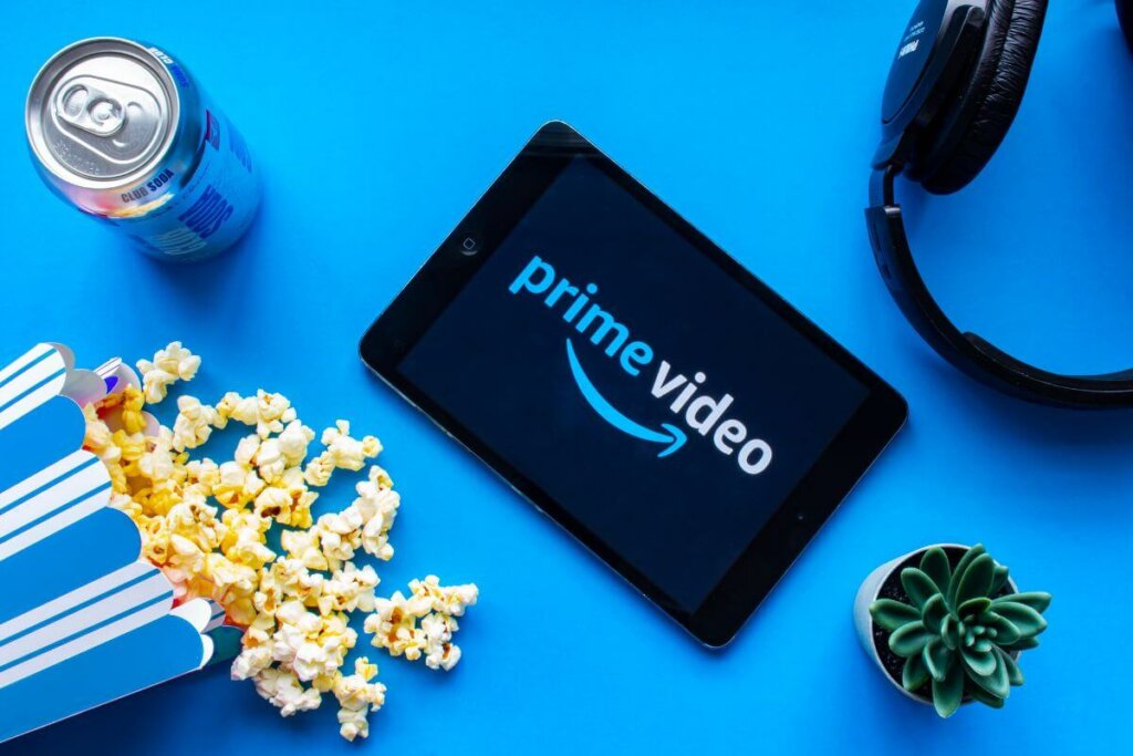 Prime video em tablet em cima de mesa com fundo azul e pipoca, refrigerante, planta e fone de ouvido