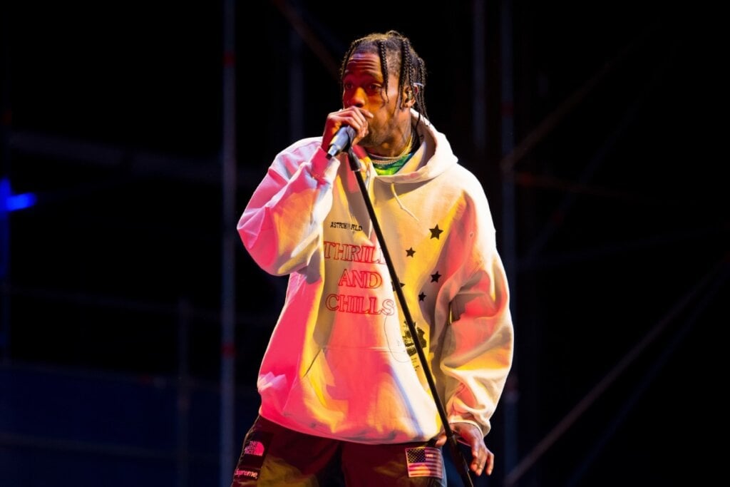 Travis Scott vestindo um moletom colorido e segurando um microfone 