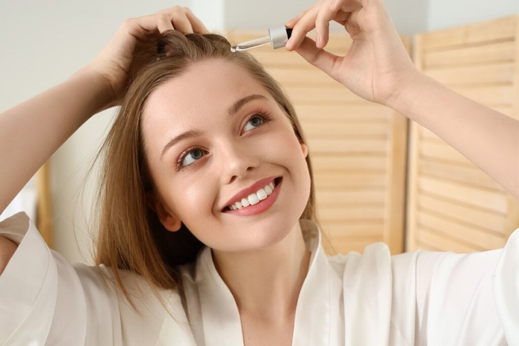 Mulher sorrindo, usando um roupão e passando óleo no cabelo 