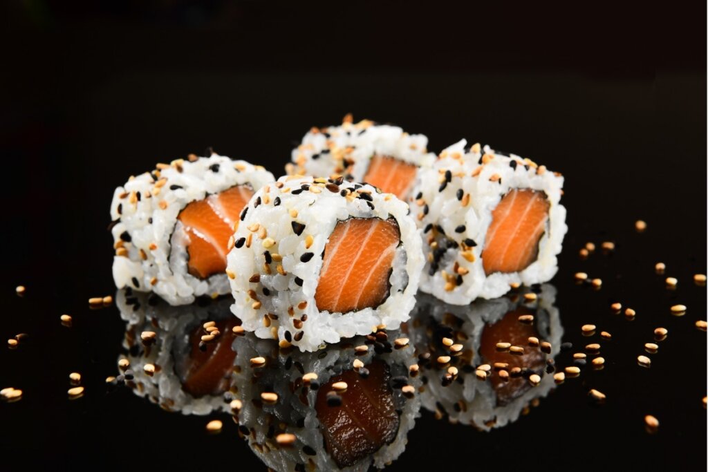 Quatro sushis Uramaki de salmão em frente a um fundo preto