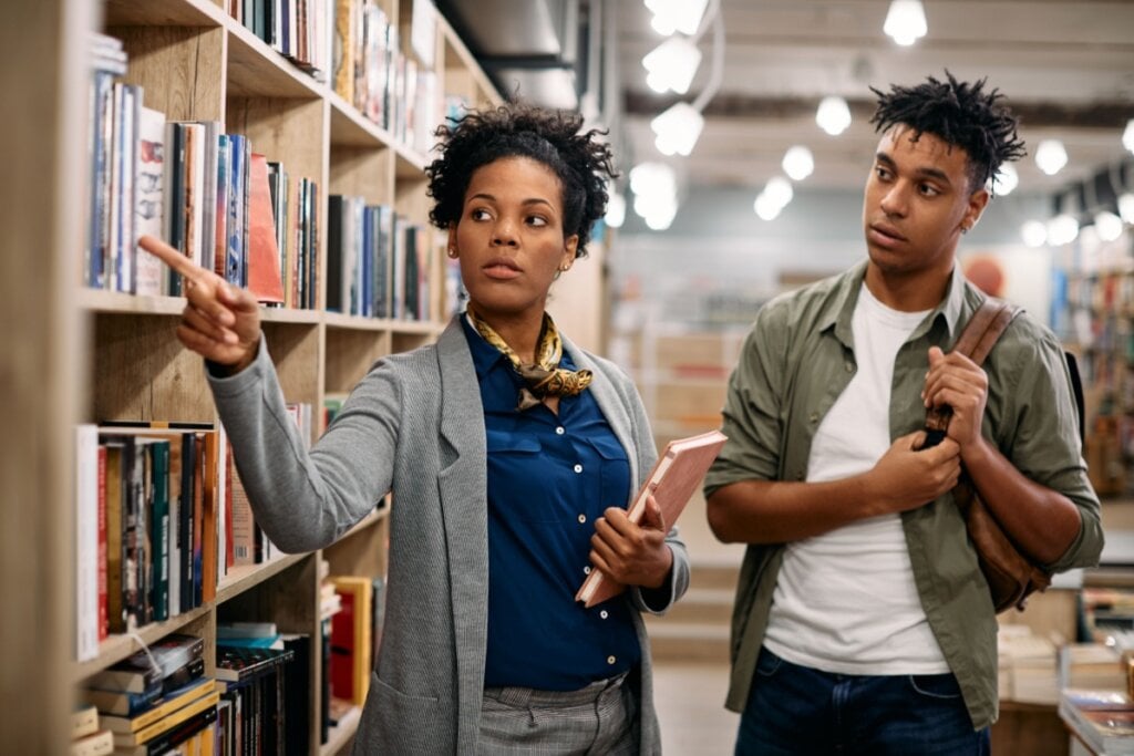 bibliotecária mostrando livros na prateleira para homem