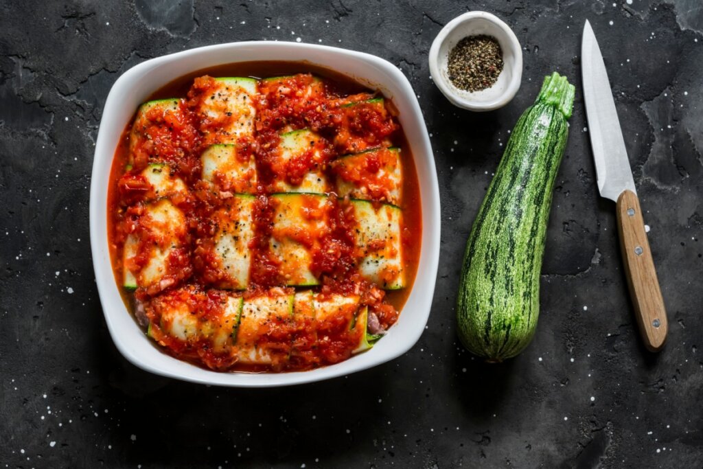 Canelones de abobrinha com ricota servido em uma forma branca, ao lado uma abobrinha e uma faca
