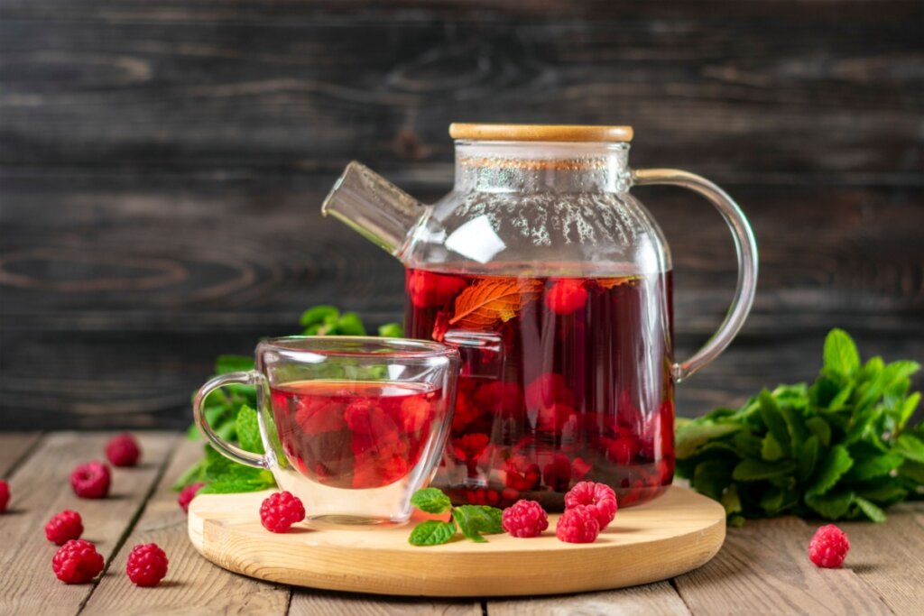 Chaleira e caneca de vidro com chá de framboesa com hortelã