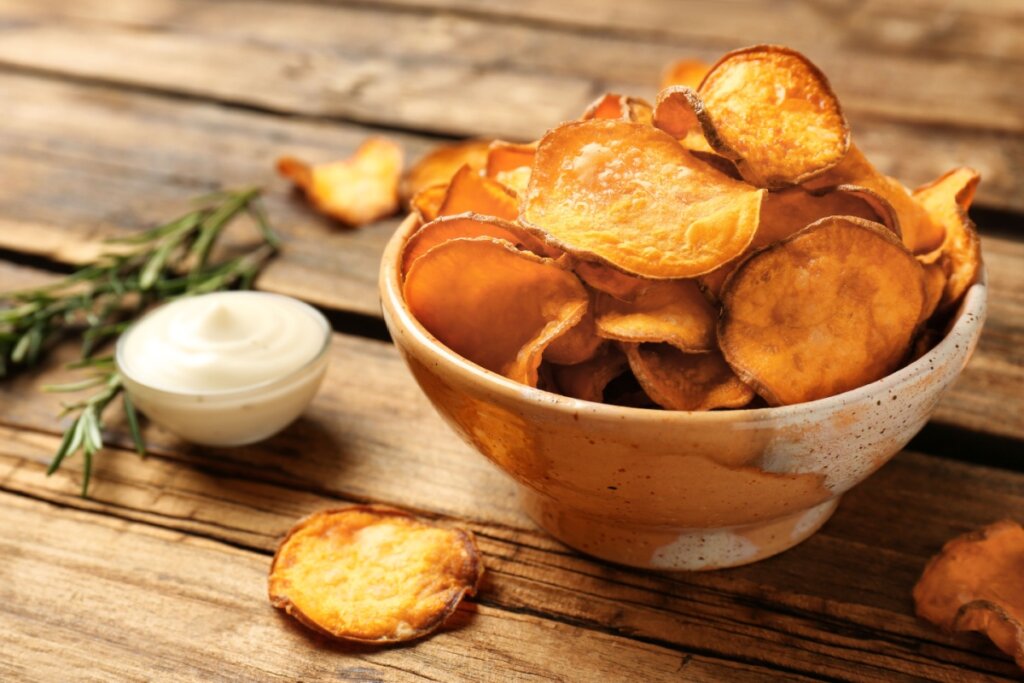 Recipiente com chips de batata-doce e, ao lado, molho e ramo de alecrim