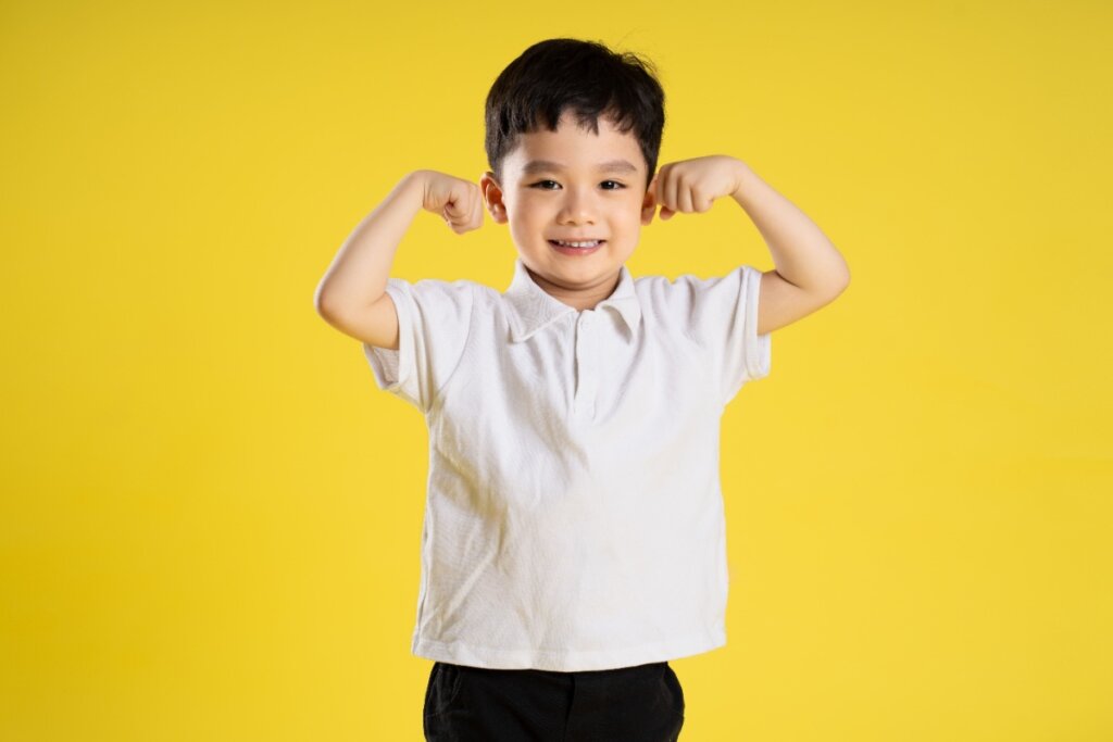 Uma criança saudável flexionando os músculos, sorrindo confiante