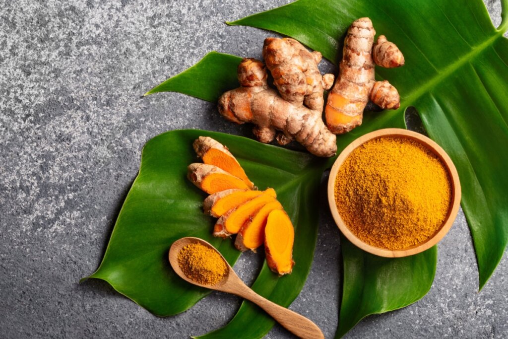 Raiz de cúrcuma, cúrcuma em pedaços e em pó em cima de folha verde