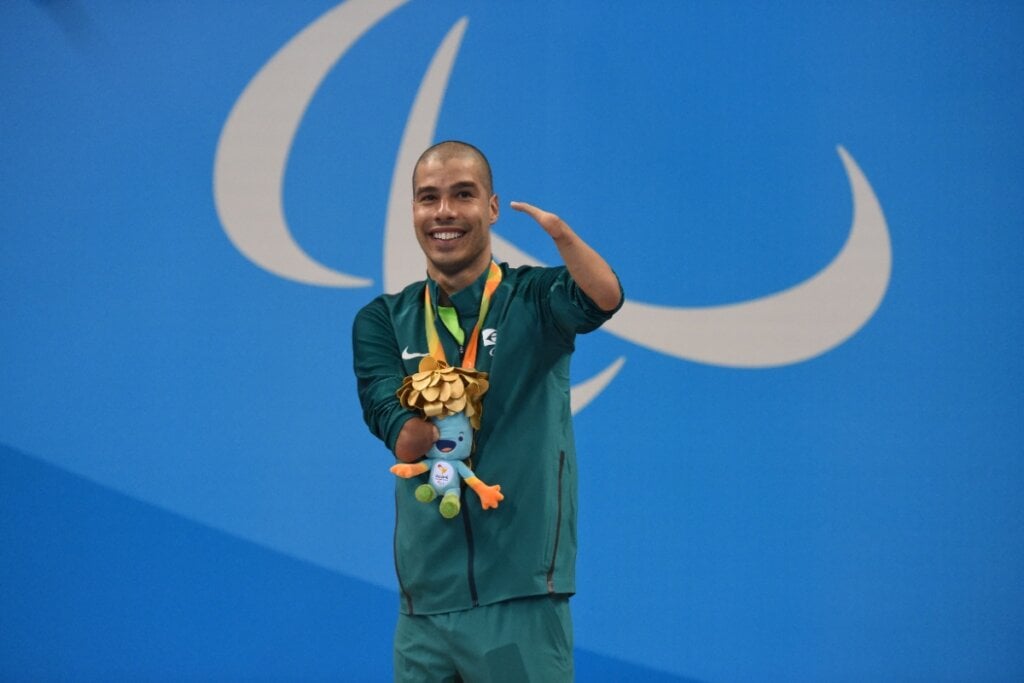 Daniel Dias, atleta de natação paralímpica, trajado de roupa verde e em fundo azul