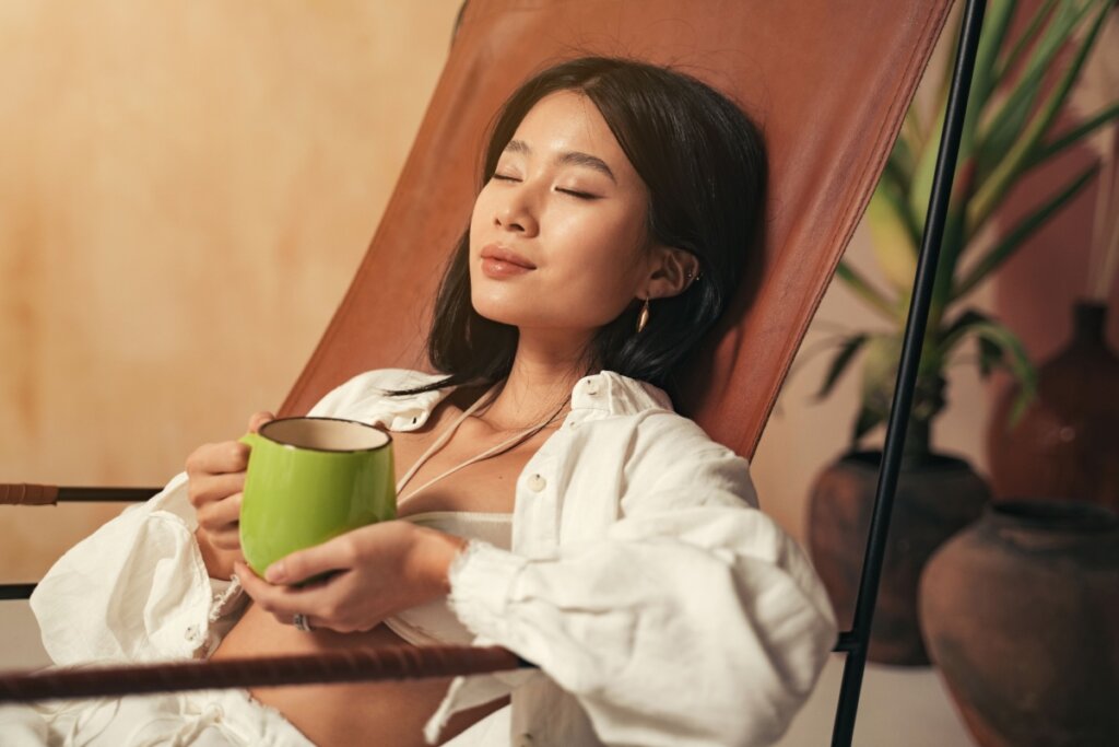 Mulher segurando xícara verde e descansando, com semblante calmo