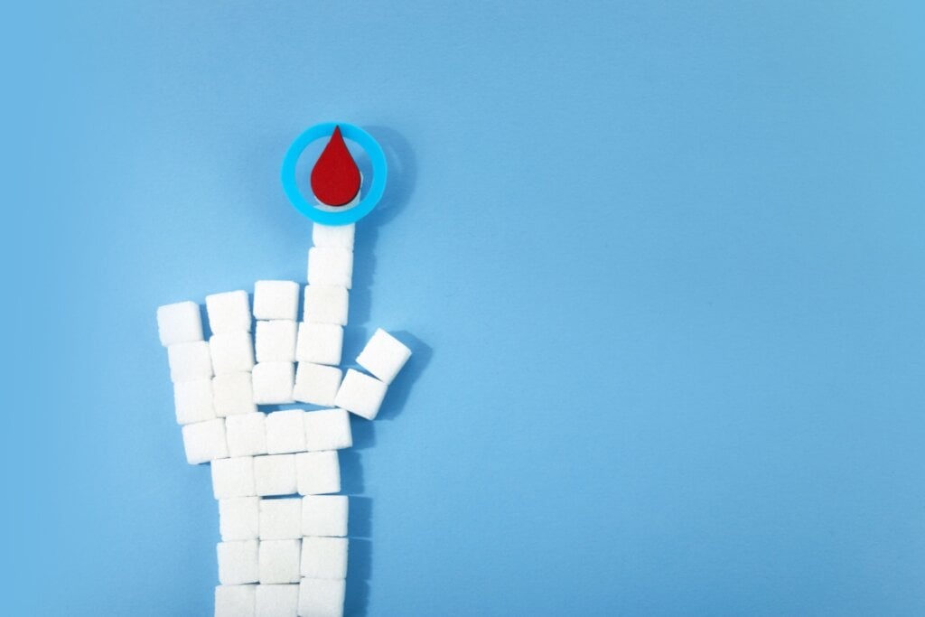 blocos de açúcar formando um antebraço e uma mão segurando uma gota de sangue em um fundo azul