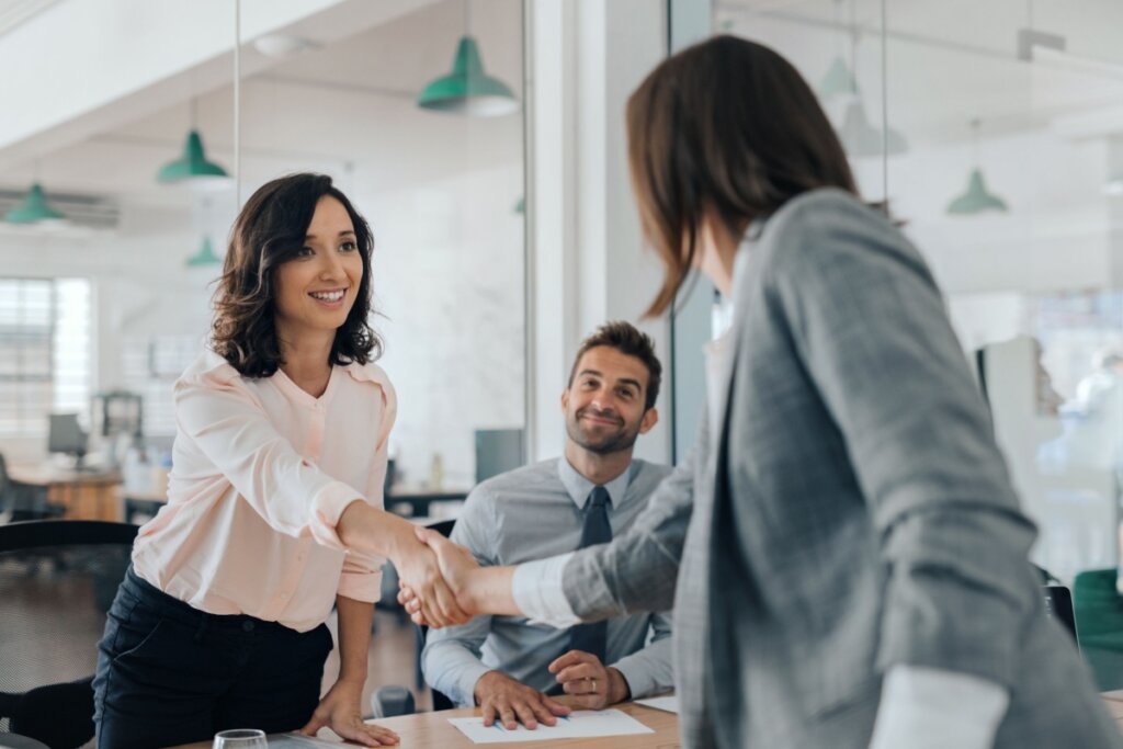 Mulher participando de entrevista de emprego e dando a mão à funcionária da empresa