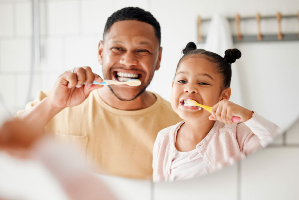 homem adulto e criança escovando os dentes olhando para o espelho