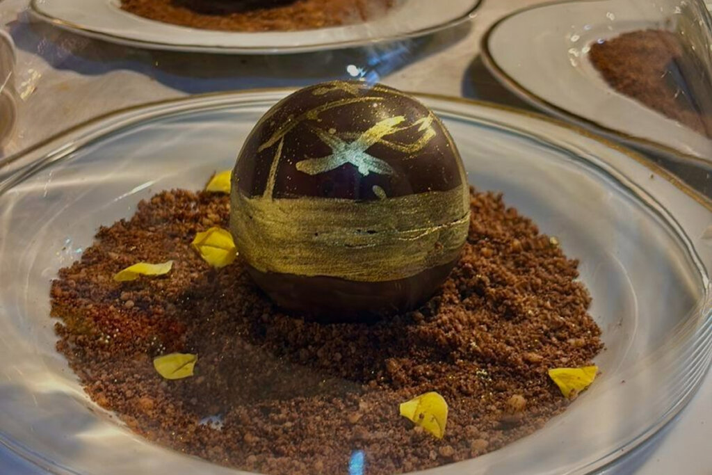 Esfera de chocolate recheada servida em prato branco com crumble de chocolate