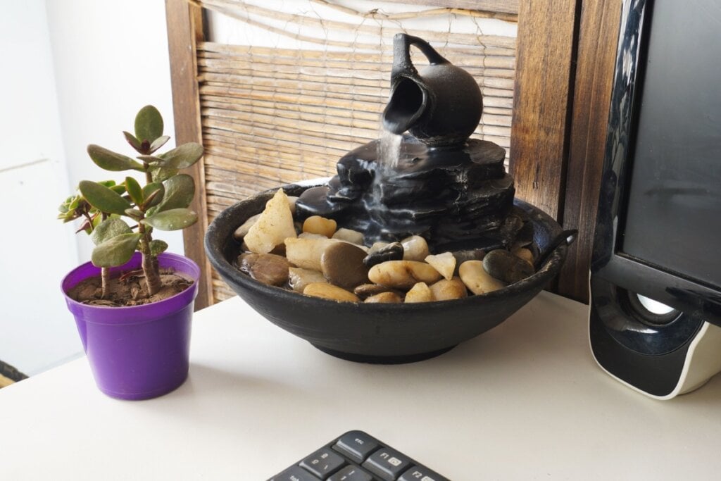 Fonte de água preta com pedra em cima de mesa e ao lado de vaso com planta