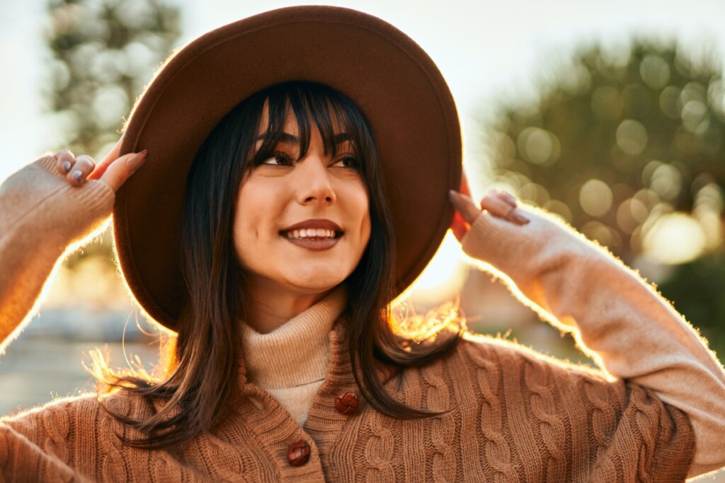 Moça de franja sorrindo com mãos no chapéu