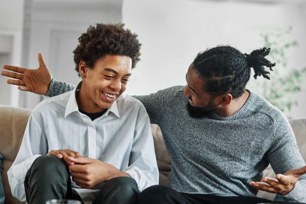 homem e adolescente em sofá conversando de forma alegre