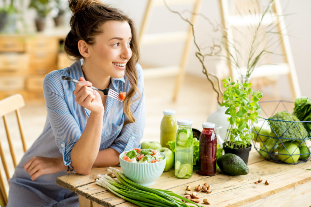 mulher sorrindo sentada em cadeira com mesa comendo salada