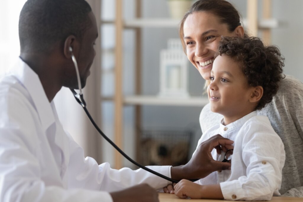 Médico ouvindo o pulmão de criança que está sentada no colo da mãe