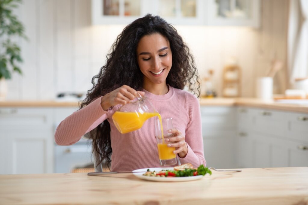 Mulher segurando jarra e colocando suco de laranja em copo