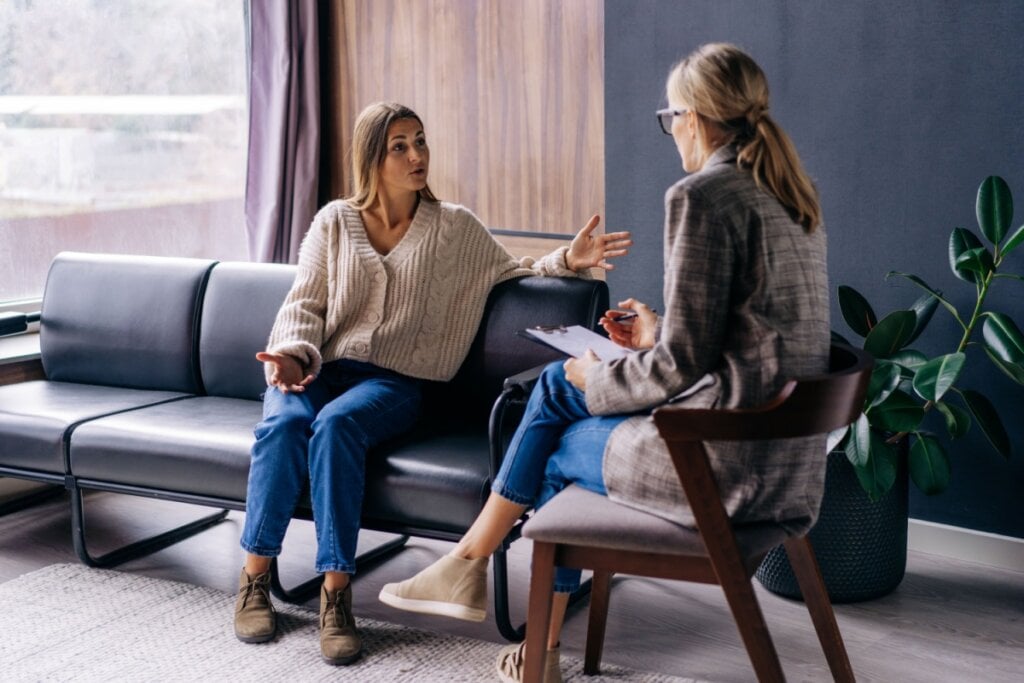 mulher na terapia sentada em sofá conversando com psicóloga na cadeira