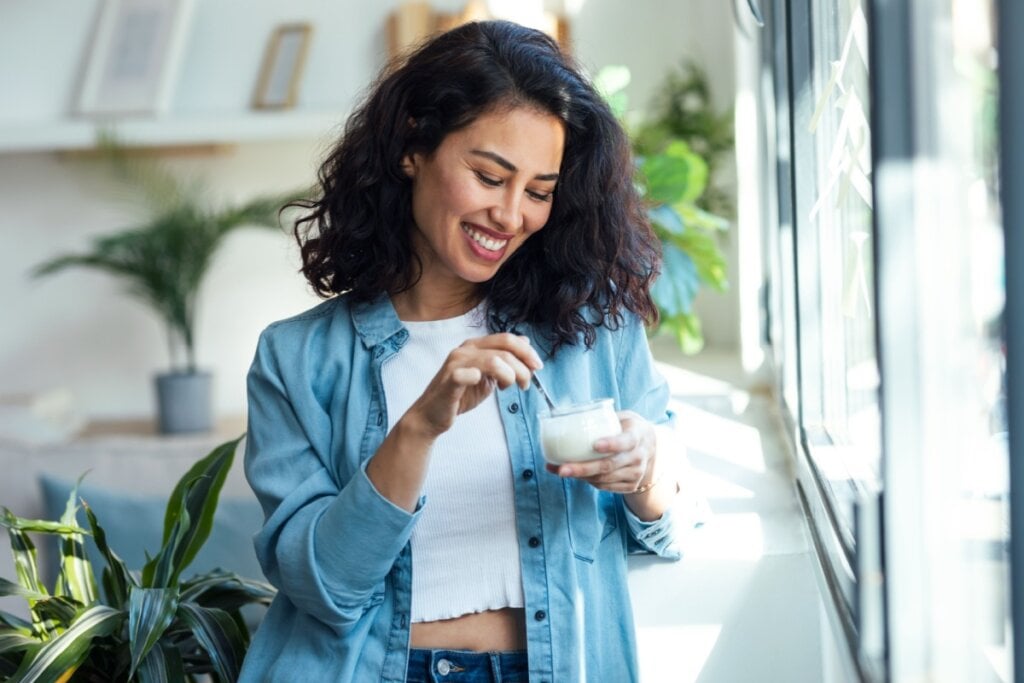 Mulher comendo iogurte natural com uma expressão feliz