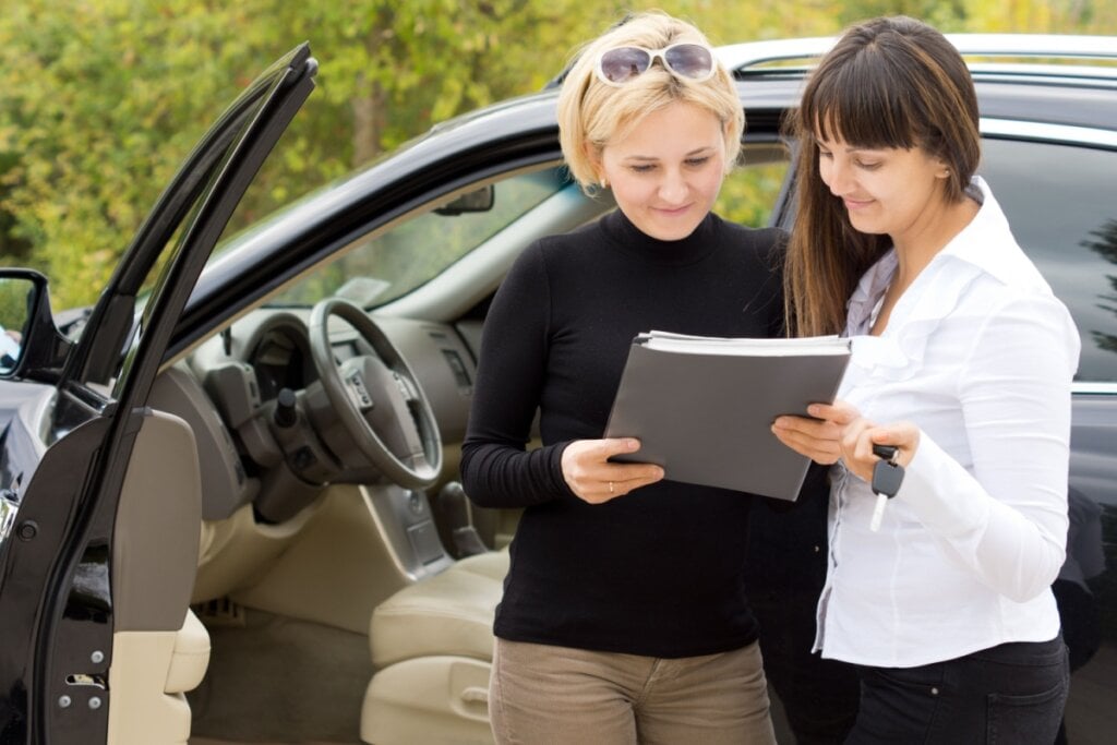 Duas mulheres conversando sobre a documentação do carro ao lado do carro 