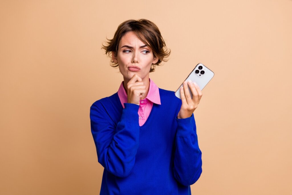 Mulher segurando o celular com uma cara de dúvida