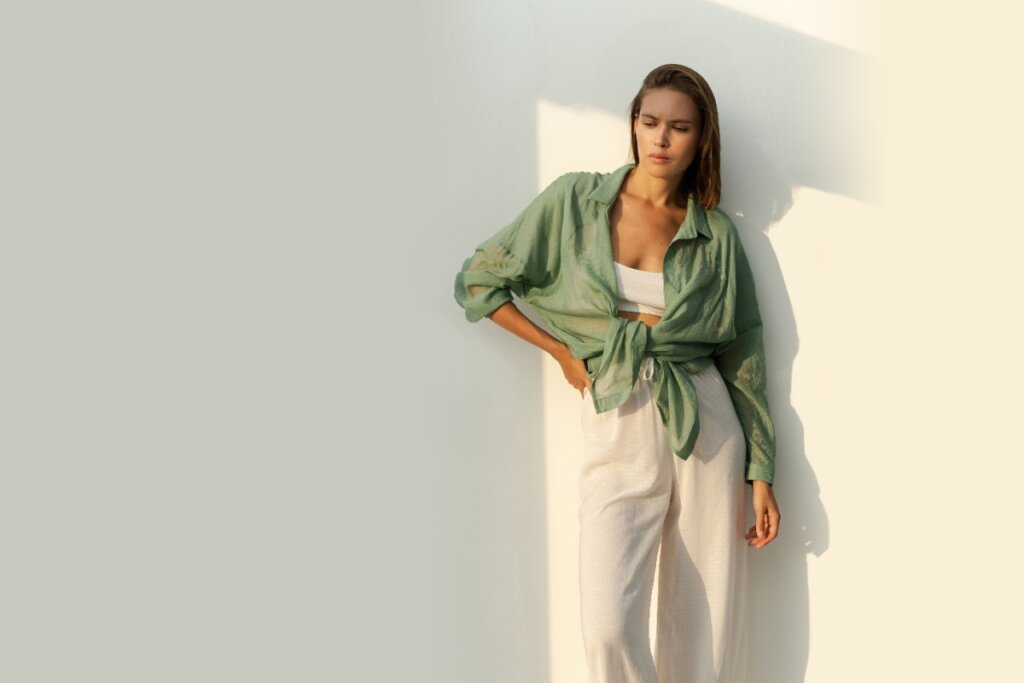 Mulher usando uma camisa verde amarrada em cima de top branco e calça em tons neutros