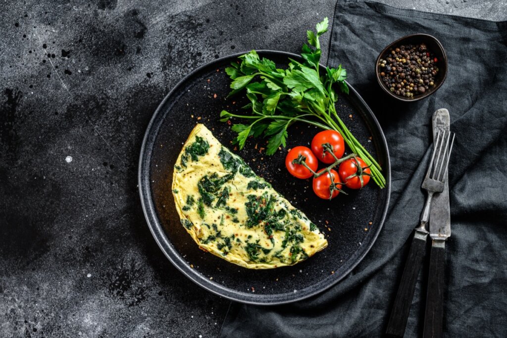 Omelete de ora-pro-nóbis servido em um prato de cerâmica preto com tomates e cheiro verde.