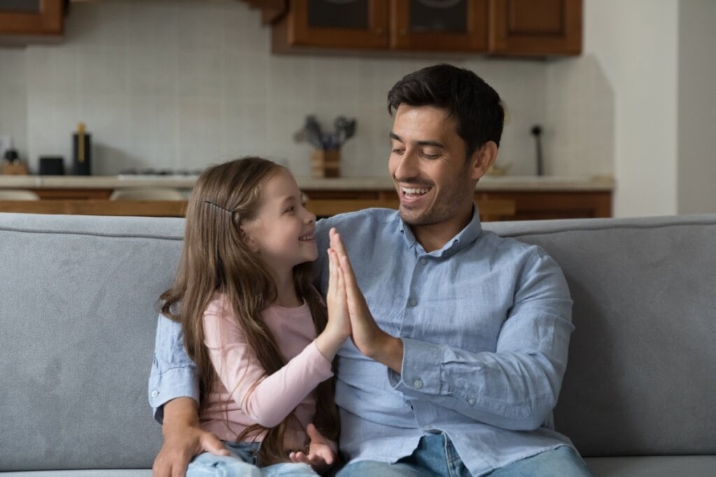 pai e filha sentados no sofá encostando as mãos em 