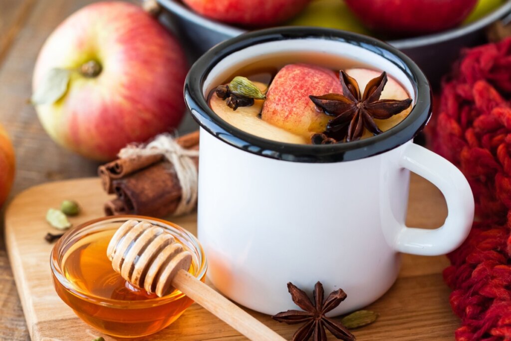 Ponche de frutas servido em caneca ao lado de um pote com mel e maçã