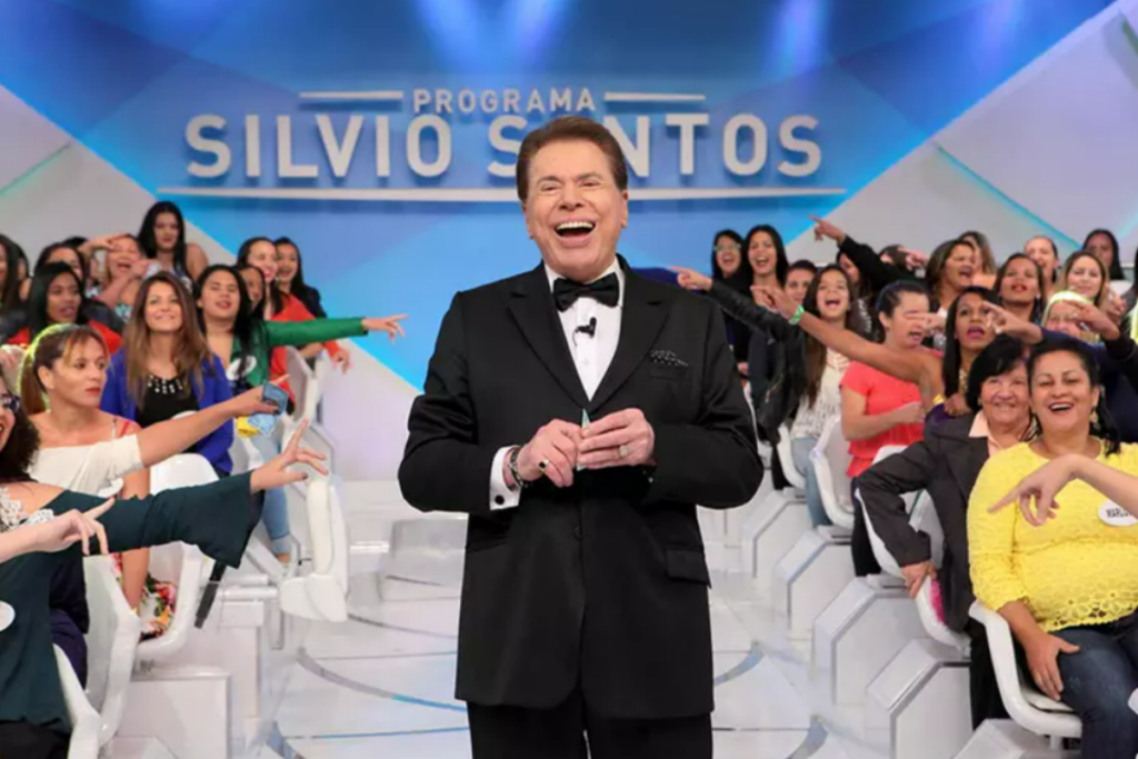 Silvio Santos sorrindo no centro da imagem e plateia ao fundo