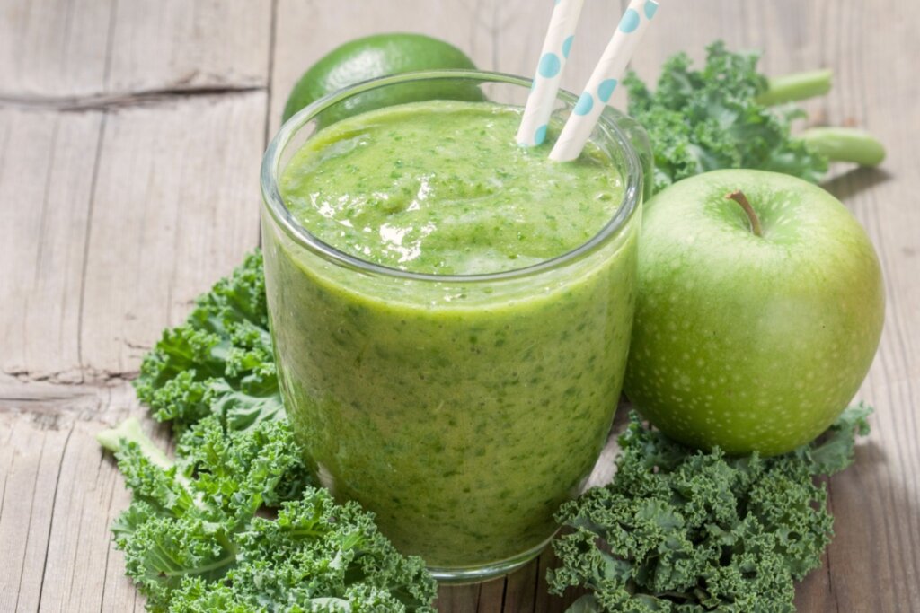 suco verde em copo de vidro com canudo e couve, maçã-verde e limão em volta