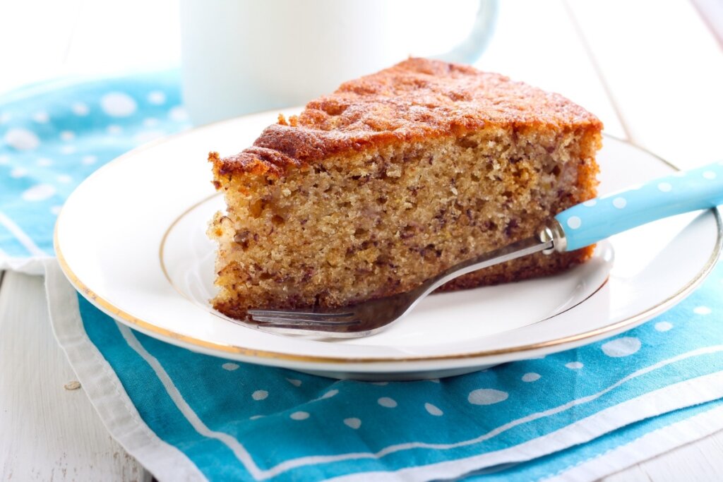 Fatia de bolo de banana em prato branco com garfo em cima de pano azul