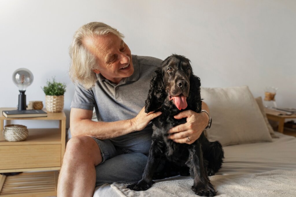 Homem sorrindo sentando em uma cama abraço um cachorro