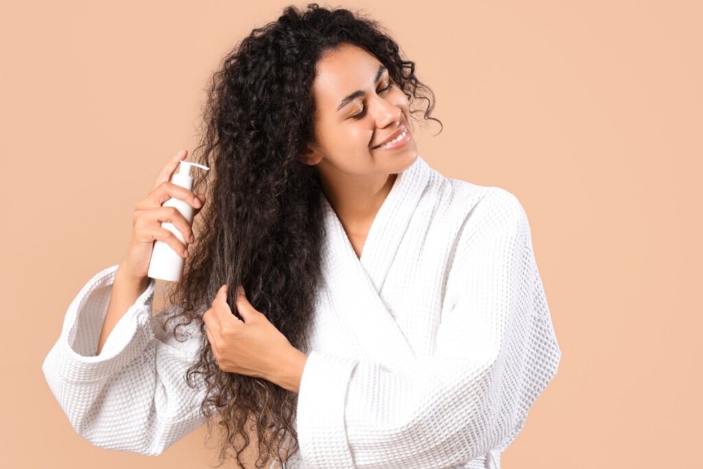 Mulher sorrindo e usando roupão passando produto no cabelo