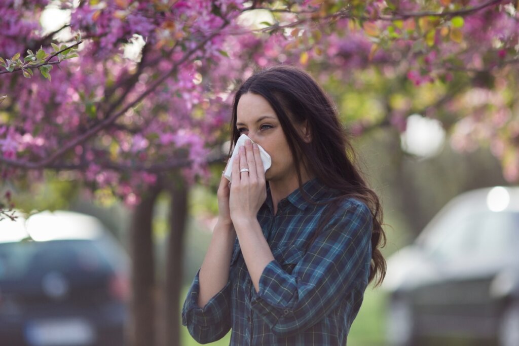 Mulher em frente a uma árvore com flores rosa assoando o nariz