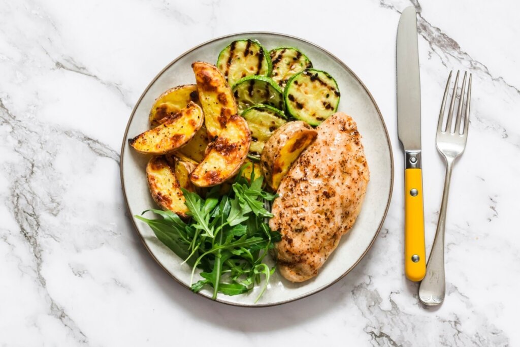 Prato branco com frango, batatas, abobrinha e rúcula