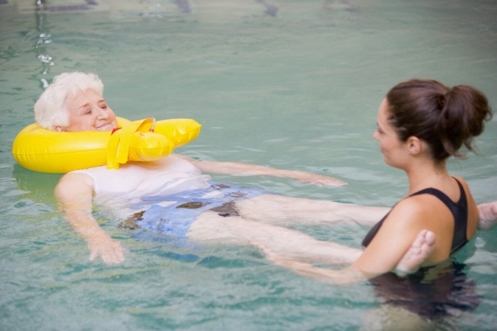 Instrutora ajudando uma idosa dentro de uma piscina 